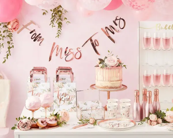 Uroczy wystrój na wieczór panieński: tort, balony, napisy "From Miss To Mrs", torby "Team Bride" i kieliszki z różowym napojem. Idealne pomysły, co robic na panieńskim!