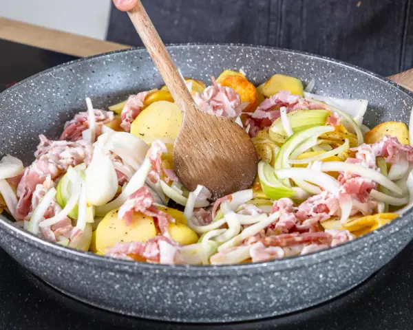 Zutaten für einen herzhaften Hamburger Pannfisch werden in einer Pfanne vermischt: Kartoffeln, Speck und Zwiebeln.