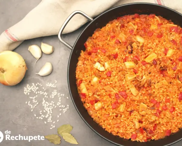 Arroz con calamares en paellera, con ingredientes como cebolla, ajo y pimientos. Un plato delicioso y lleno de sabor.