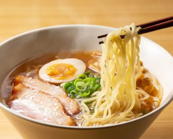 Parujące miseczka ramenu z makaronem, plastrami mięsa, jajkiem i szczypiorkiem. Idealne ramen przyprawy podkreślają smak.