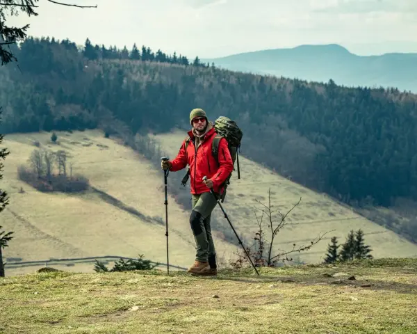 Mężczyzna w czerwonej kurtce i z plecakiem, gotowy do nordic walking. Jak zacząć? Wskazówki dla początkujących.