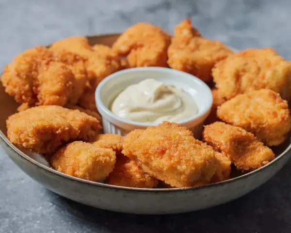 En skål med gyllene, krispiga chicken nuggets och en liten skål med krämig dippsås. Perfekt för en snabb och god måltid.