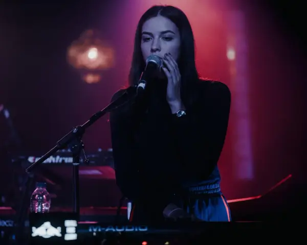 Wokalistka na tle sceny, przygotowująca się do występu na jednym z festiwali muzyki elektronicznej w Polsce.