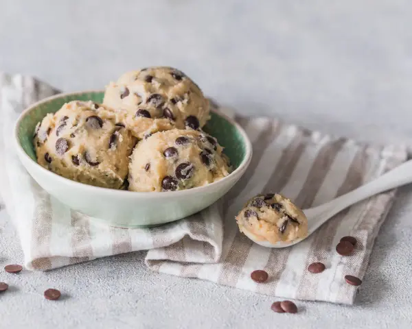 Schüssel mit köstlichem Cookie-Teig ohne Ei und Schokostückchen, bereit für den Ofen. Ein Löffel voll Teig liegt daneben.