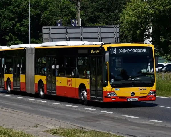 Autobus 114 jedzie ulicą w słoneczny dzień.