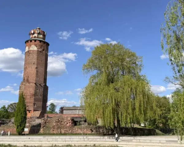 Wieża zamkowa w Brodnicy, otoczona zielenią, na tle błękitnego nieba z chmurami. Piękny dzień na Pojezierzu Brodnickim.