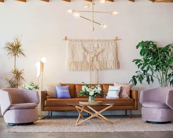 Salon moderne avec canapé en cuir marron, fauteuils roses poudrés, tapis texturé et macramé mural. La couleur peinture salon est neutre, mettant en valeur les meubles.