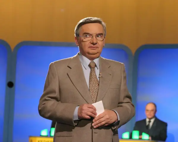 Tadeusz Sznuk, który prowadzi teleturniej Jeden z dziesięciu, w beżowej marynarce i z kartką w dłoni.
