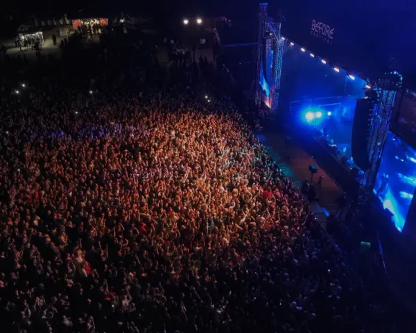 Tłum ludzi na koncercie, rozświetlony sceną i światłami. Atmosfera przed festiwalem Before Festival jest elektryzująca.