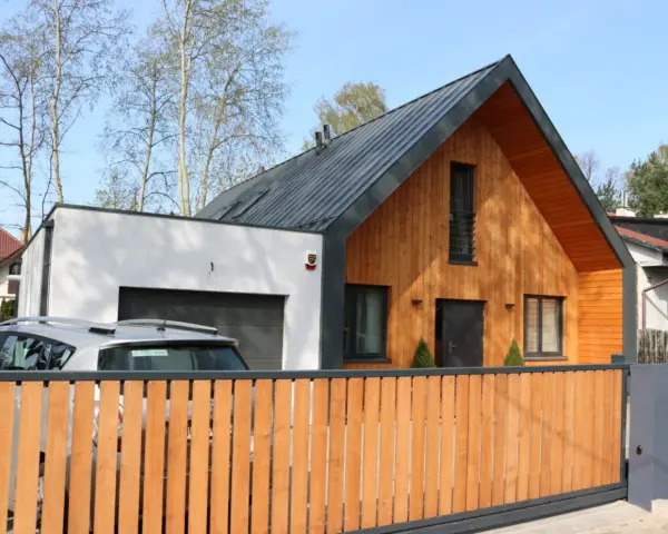 Nowoczesny dom z drewnianą dobudówką do części murowanej. Obok garaż, przed którym stoi samochód.