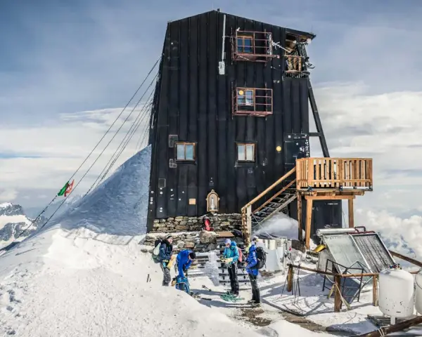 Die Capanna Margherita, eine Berghütte auf einem schneebedeckten Gipfel, mit Bergsteigern, die sich auf den Aufstieg vorbereiten.
