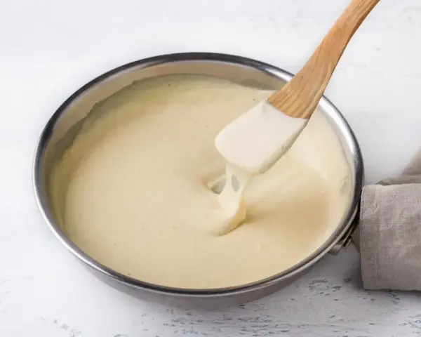 Una spatola di legno mescola una cremosa fonduta di parmigiano in una padella.