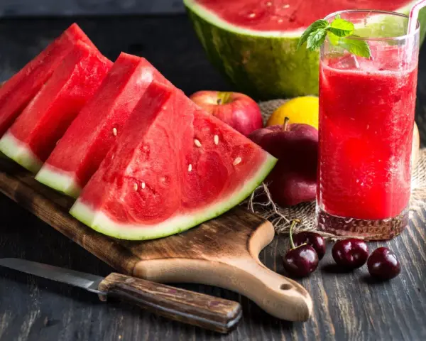 Saftige Wassermelone-Scheiben und ein Glas erfrischender Wassermelonensaft, reich an Vitaminen. Äpfel und Kirschen ergänzen das gesunde Arrangement.