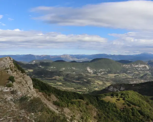 Vue panoramique depuis le col de Perty, avec des montagnes verdoyantes et un ciel bleu parsemé de nuages.
