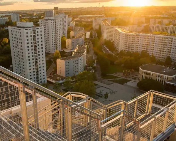 Blick von einer Treppe auf den Skywalk Marzahn bei Sonnenuntergang. Hohe Wohnhäuser und grüne Flächen prägen die Szenerie.