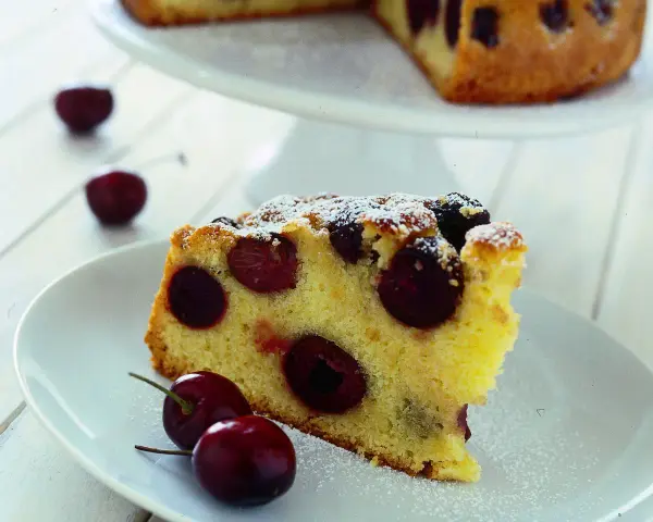 Una fetta di torta soffice e dorata, ricca di ciliegie succose, cosparsa di zucchero a velo. Perfetta per un momento di dolcezza.