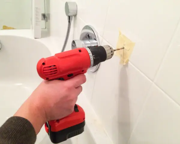 Bohren von Fliesen im Badezimmer mit einem roten Akkuschrauber. Ein Stück Klebeband schützt die Wand.