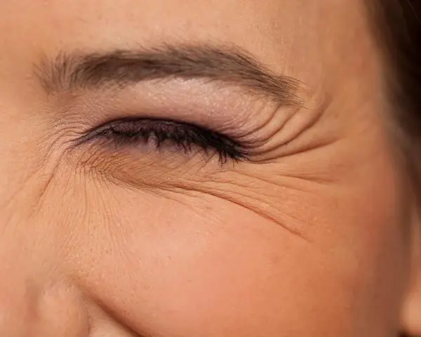 Primer plano de un ojo cerrado con maquillaje, mostrando las arrugas debajo de los ojos que marcan la expresión.