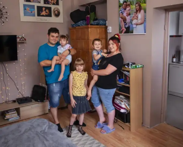 Rodzina z trójką dzieci pozuje do zdjęcia w salonie. W tle widać zdjęcia, telewizor i ozdobne lampki. Ich życie na kredyt nie przeszkadza im w cieszeniu się chwilą.