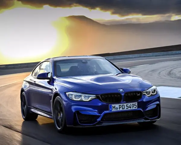 Niebieskie BMW M2 CS pędzi po torze wyścigowym podczas zachodu słońca.