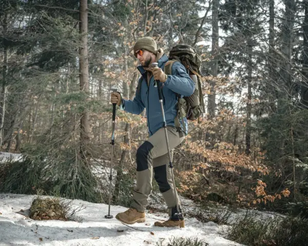 Mężczyzna w zimowej kurtce i czapce idzie przez las, używając kijków do nordic walking. Wskazówka, jak dobrać kije do nordic walking, jest kluczowa dla komfortu.