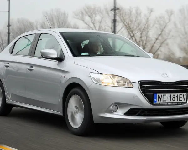 Srebrny Peugeot 301 jedzie po drodze, za kierownicą siedzi mężczyzna w okularach.
