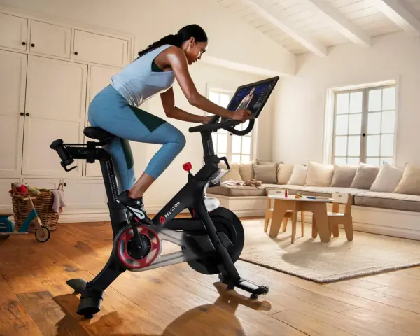 A woman rides a Peloton bike, a popular tool for peloton weight loss, in a bright, homey living room.