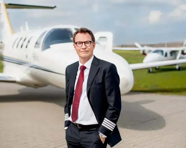 Pilot w garniturze z odznaką na rękawie, stojący przed odrzutowcem. Zastanawiasz się, ile zarabia pilot Ryanair?