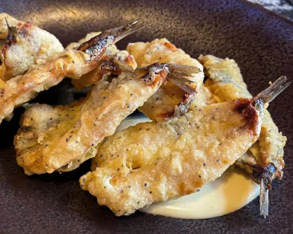 Crujientes boquerones fritos, dorados y servidos sobre una cremosa salsa.