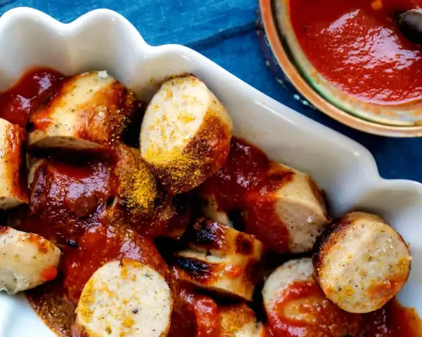 Leckere Currywurst mit einer würzigen Currywurst-Sauce und Currypulver bestreut, serviert in einer weißen Schale.