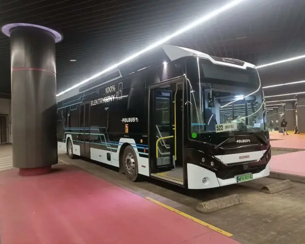 Nowoczesny, czarny autobus elektryczny z napisem "100% ELEKTRYCZNY" stoi na przystanku.