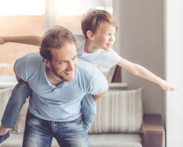 Ein Vater trägt seinen Sohn auf dem Rücken. Der Sohn streckt die Arme aus wie ein Flugzeug. Das sind meine worte an meinen sohn: Flieg hoch!