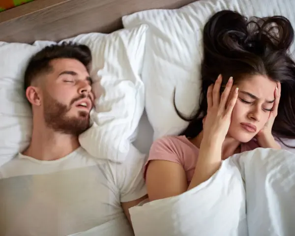 Kobieta zatyka uszy, próbując zasnąć obok męża, który głośno chrapie. Może czas na wizytę u lekarza od chrapania?