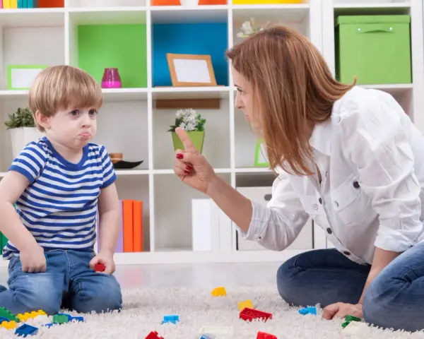 Mama karci synka za kłamstwo. Chłopiec ma smutną minę, a na dywanie leżą klocki.