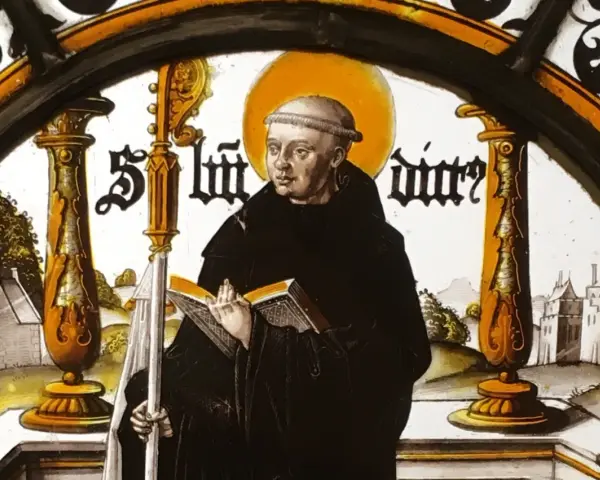 Stained glass depicting St. Benedict the Abbot, holding a book and staff, with a monastery in the background.