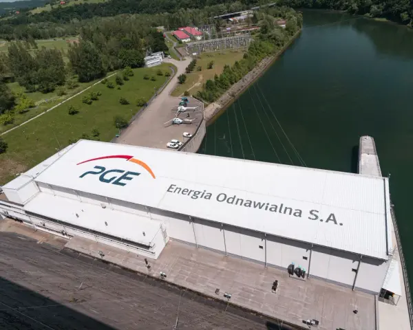 Widok z lotu ptaka na elektrownię wodną PGE Energia Odnawialna S.A. z charakterystycznym logo. Widać tam też helikoptery i samochody.