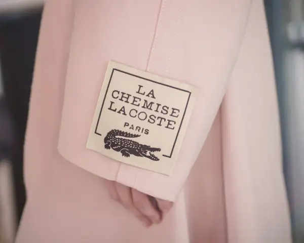 Różowy płaszcz z metką "LA CHEMISE LACOSTE PARIS" z krokodylem, symbol luksusowych marek ubrań.