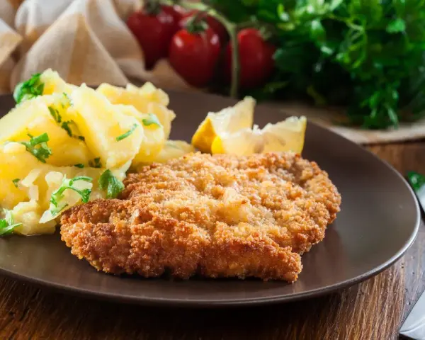 Kotlet schabowy w panierce z ziemniakami i cytryną na brązowym talerzu.