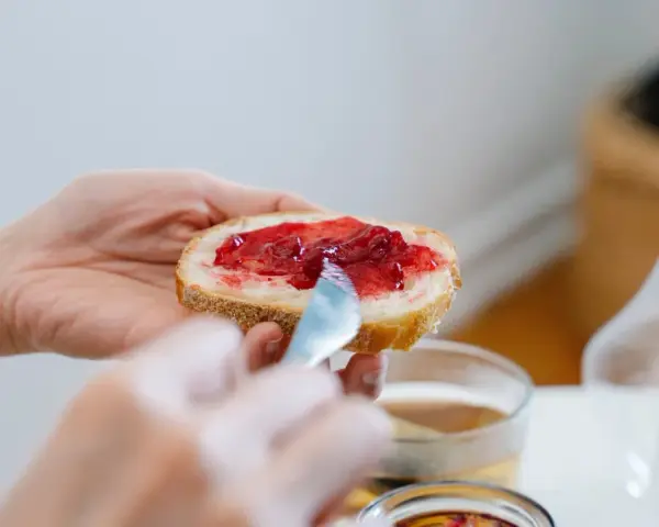 Hände verteilen Marmelade auf Brot. Ein süßer Genuss, der an die besonderen Gelüste in der Schwangerschaft erinnert.