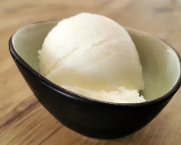 Ein Löffel cremiges Sorbet ohne Zucker in einer stilvollen Schale auf Holzhintergrund. Erfrischend und leicht.