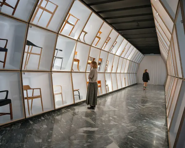 Wystawa krzeseł w muzeum designu Kopenhaga. Ludzie podziwiają ekspozycję w nowoczesnej, geometrycznej przestrzeni.