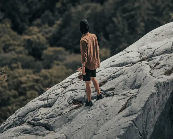 Un homme sur un rocher escarpé, le regard perdu dans le lointain, semble lutter contre sa peur du vide.