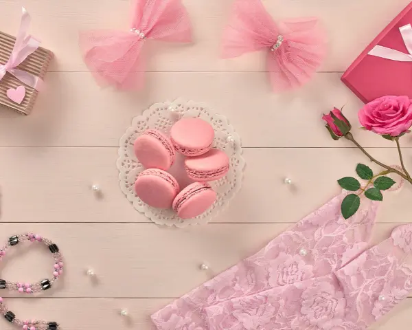 Różowy symbolika: delikatne kokardki, słodkie makaroniki, róża i koronka tworzą romantyczną kompozycję.