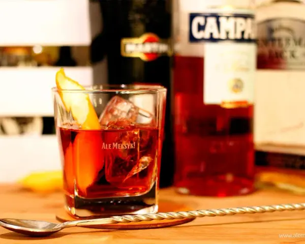 Klasyczny drink z pomarańczą i lodem. Wybór między Negroni czy Boulevardier? Na stole widać butelki Martini, Campari i Jack Daniel's.