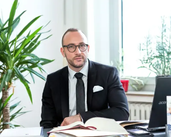 Ein Mann im Anzug sitzt am Schreibtisch, umgeben von Pflanzen. Er ist ein erfahrener Rechtsanwalt für Scheidungsrecht.