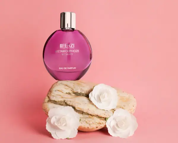 Różowa butelka perfum JFenzi Mon Amie Metamorphoze Women na kamieniu z białymi kwiatami.