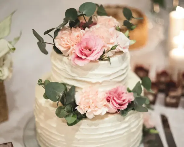 Elegancki tort weselny z kremową dekoracją i pastelowymi kwiatami, ozdobiony gałązkami eukaliptusa.