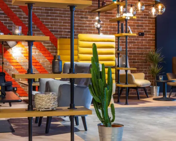 Nowoczesne wnętrze lobby hotelu Radisson Hotel Poznań Park Inn: ceglana ściana, żółte i szare fotele, regały z dekoracjami i kaktus.