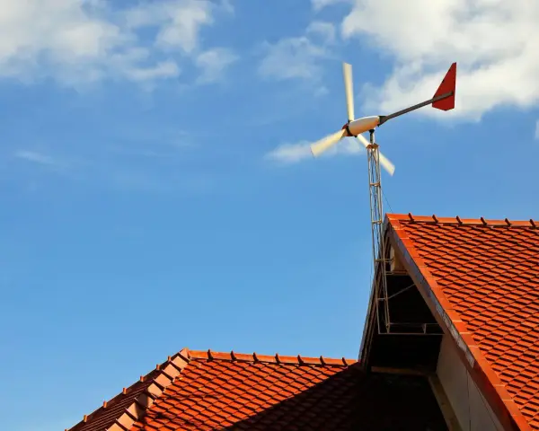Mała elektrownia przydomowa na tle błękitnego nieba z chmurami. Wirnik turbiny wiatrowej obraca się, dostarczając czystą energię.