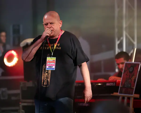 Kazik Staszewski śpiewa na koncercie, ubrany w czarną koszulkę z napisem "Kwartet Pro Forma" i identyfikatorem "Zespół KULT".